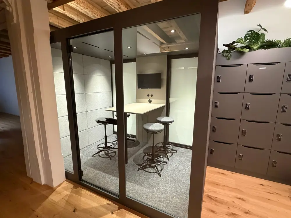 Glazed silent room at G3ckarium with bar stools, next to the locker wall with a plant